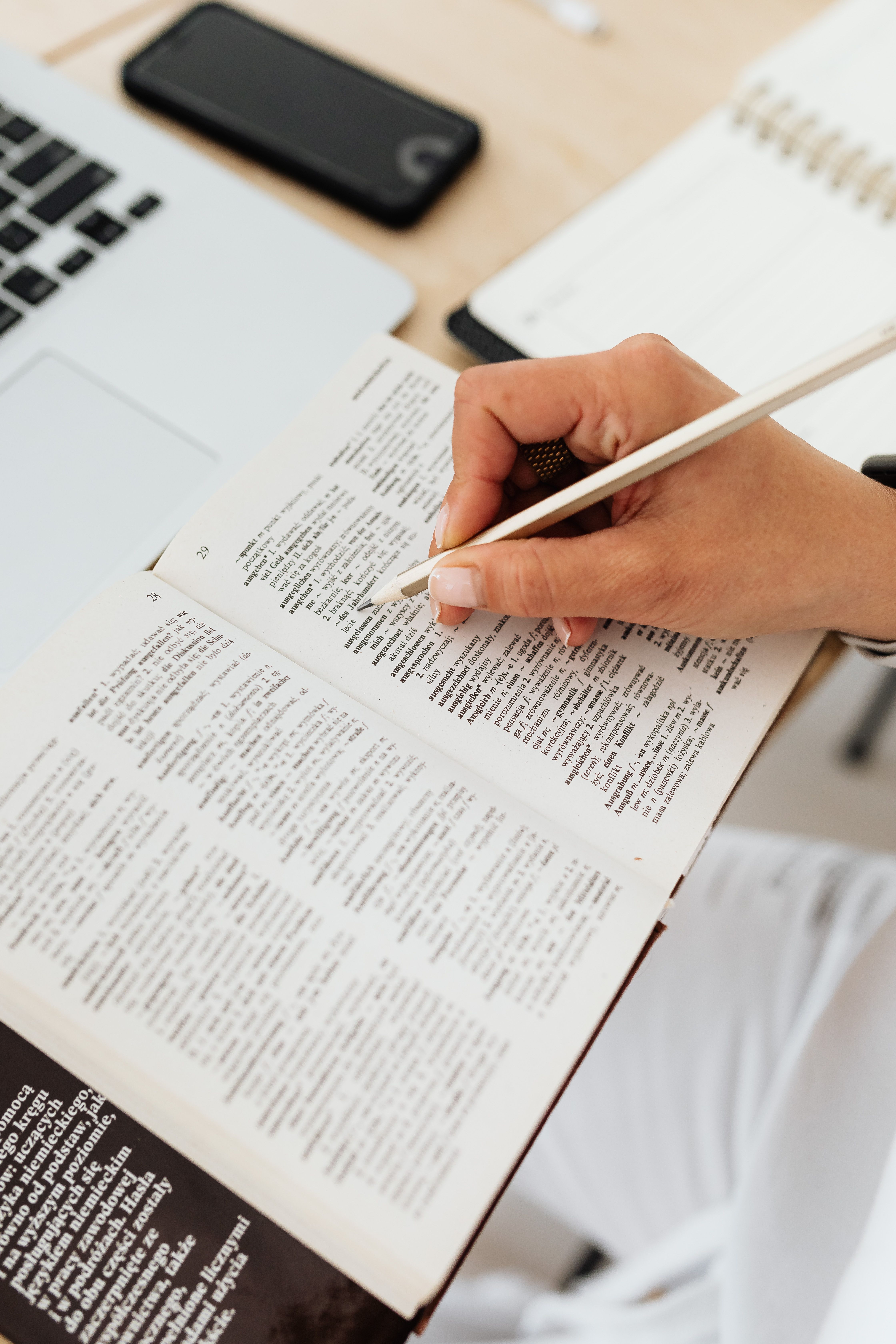 A learner marking useful vocabulary in a book beside a laptop and notebook.
